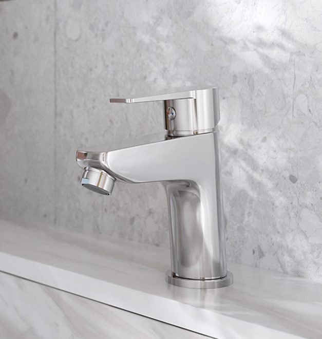 Chromowana bateria umywalkowa Ferro Ritto stojąca na białym blacie, na tle szarej, marmurowej ściany.